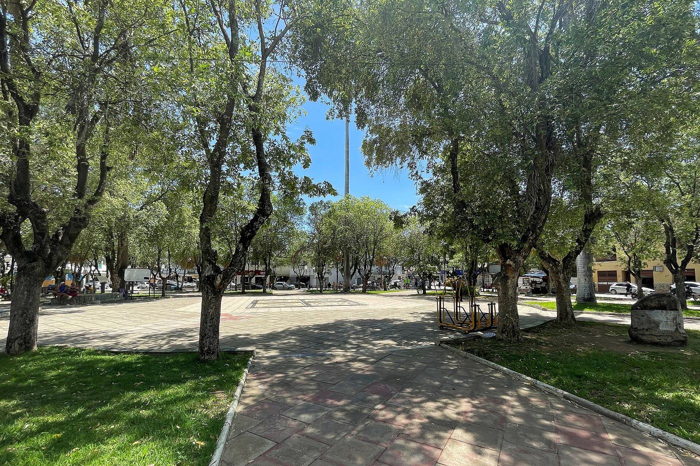 Praça central de uma cidade do interior de Minas Gerais, com bancos, árvores e igreja ao fundo